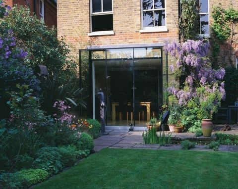 Pemandangan halaman dan belakang rumah dengan kolam persegi panjang, wisteria, dapur berhias kaca dan patung oleh Helen Sinclair