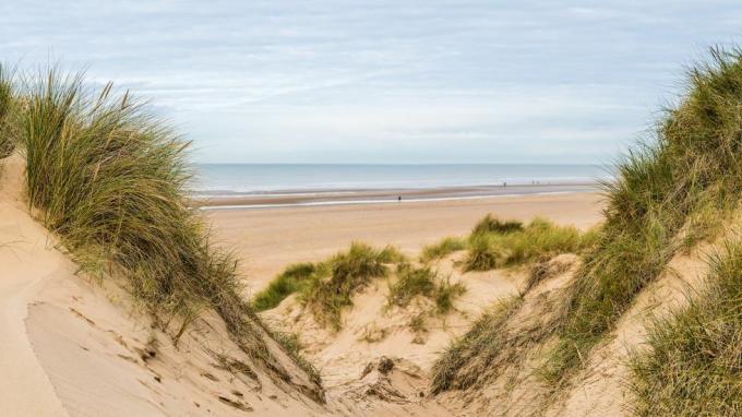 panorama multi-gambar yang diambil di antara dua puncak di bukit pasir sambil memandangi orang-orang yang berjalan di sepanjang pantai formby dekat liverpool