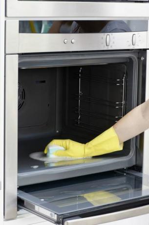 Wanita mengenakan sarung tangan cuci kuning untuk membersihkan di dalam oven menggunakan spons