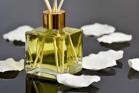 Vanilla beraroma reed diffuser penyegar udara dan kelopak mawar di permukaan reflektif.