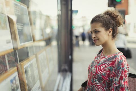 Wanita muda menelusuri daftar real estat di etalase kota