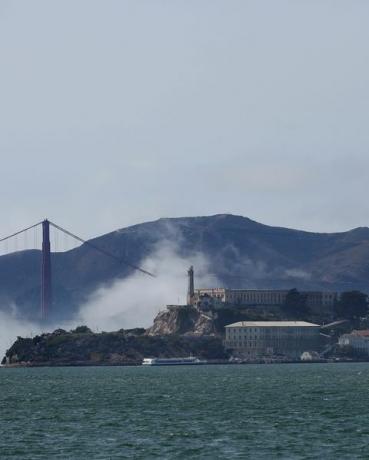 kabut rendah berputar di sekitar alcatraz dan jembatan golden gate di bawah langit cerah saat kapal berlayar di teluk san francisco