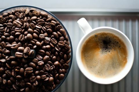 Biji kopi segar dalam penggiling, selain secangkir kopi hitam segar