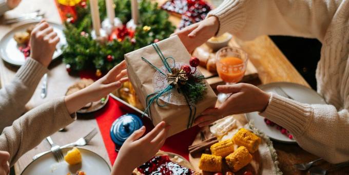 tampilan atas dari orang tua penuh kasih yang tidak dapat dikenali memberikan kotak meriah dengan hadiah Natal untuk anak bahagia yang duduk di meja pesta makan malam